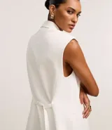 Chaleco largo de sastrería color blanco, con solapas tipo peaked, cierre frontal oculto y ajuste mediante lazo con hebilla en la espalda.