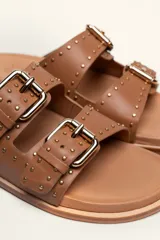 Sandalias de cuero color negro con dos tiras anchas sobre el empeine, cada una con hebillas metálicas ajustables y detalles de tachas plateadas. La suela es de cuero con un borde de color madera.