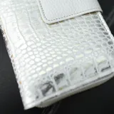 Billetera blanca con textura croco, cierre con broche y correa de mano.