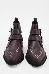 Botín de cuero vacuno color marrón, con punta fina y detalle de tachas metálicas en la parte superior. Presenta una suela de plataforma plana de color negro.