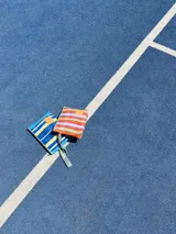 Sobre de mano azul con rayas verticales blancas y amarillas, con parche de cuero sintético marrón.