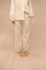 Pantalón Anel de corte recto y holgado, color blanco, confeccionado en tela con diseño bordado o broderie con motivos florales y detalles calados en toda la prenda, incluyendo los bolsillos laterales y el ruedo.