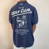 Chomba de corte oversize color beige, con cuello polo y cierre frontal de botones. Presenta bordados en el pecho con motivos de golf y tipografía cursiva.
