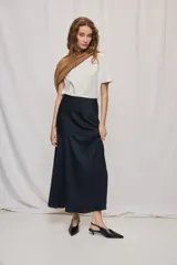 Falda larga de color negro, calce al cuerpo y caída fluida, confeccionada en tejido satinado con detalle de recorte diagonal en la parte delantera y cintura elástica.