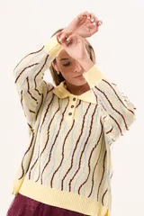 Buzo de punto tipo polo en tono amarillo claro con diseño de ondas a rayas en tonos marrón y celeste. Presenta cuello clásico, cierre frontal parcial con botones y silueta relajada con mangas largas.