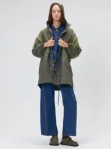 Campera tipo piloto con capucha, cierre frontal con botones y detalle de costuras en zigzag. Presenta cordones ajustables en la cintura y capucha, puños elásticos y logo bordado en el pecho.