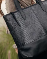 Bolso tipo tote de cuero negro con textura de reptil en la parte superior y base de cuero liso. Cuenta con doble asa de hombro.