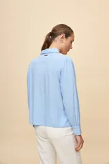 Camisa de manga larga color celeste, con cuello clásico y botonadura frontal. Presenta un calce relajado, con mangas amplias y puños anchos.