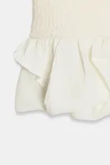 Vestido corto de color blanco con cuello redondo y diseño sin mangas. Presenta un cuerpo de tejido bouclé texturizado y un bajo acabado con volantes de tejido ligero.