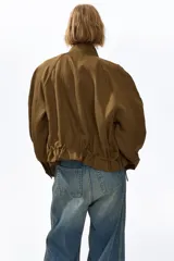 Campera corta verde militar en mezcla de lino, con cuello elevado, mangas raglán, bolsillos frontales con solapa y botones, y cordón ajustable en el bajo.