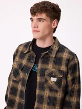 Camisa de manga larga confeccionada en franela de algodón, con diseño de cuadros en tonos verde y marrón. Presenta cuello clásico, cierre frontal con botones y dos bolsillos en el pecho con solapa.