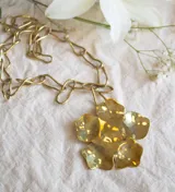 Collar dorado con cadena de eslabones grandes y dije de flor con textura irregular.