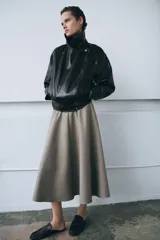 Chaqueta de estilo biker confeccionada en tejido efecto piel con acabado brillante. Presenta cuello con solapas, cierre frontal con cremallera y botones, bolsillos delanteros y bajo ajustable con trabillas y hebilla metálica.