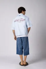 Camisa de manga corta de popelina rayada, con calce boxy y bordado sutil en el pecho. Presenta cierre frontal con botones y diseño abierto.