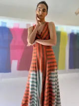 Vestido largo de lino rayado color naranja y marrón, con escote en V y espalda descubierta. La falda es amplia y con mucho movimiento.