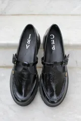 Zapato tipo guillermina en cuero charol color bordó, con suela track negra de goma, cierre con hebilla ajustable y detalle de herrajes metálicos dorados.