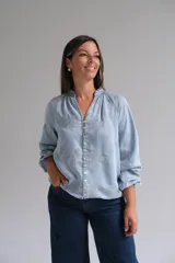 Blusa de tela tipo denim liviano en tono azul claro, con cuello mao, cierre frontal de botones y mangas largas con puños. Presenta un delicado bordado floral en todo el frente y las mangas.