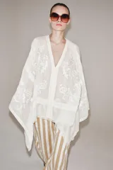 Blusa tipo capa de algodón con escote en pico y cierre frontal con botones. Presenta mangas largas amplias y diseño con bordados florales a tono, con bajo asimétrico.