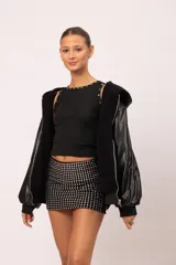 Musculosa negra entallada con cuello redondo, decorada con apliques metálicos de tachas, estrellas y ojalillos en el contorno del cuello y las sisas.