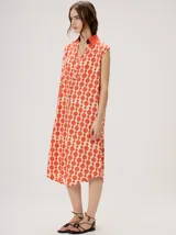 Vestido midi camisero sin mangas, de corte recto y holgado. Cuenta con cuello camisero liso en color naranja y cierre frontal parcial con botones. Presenta un estampado geométrico psicodélico en tonos naranja y beige.