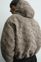 Cazadora acolchada de corte relajado con estampado jacquard. Presenta cuello subido con capucha, cierre frontal de cremallera, bolsillos frontales y puños con acabado elástico.