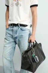 Bolso de viaje de diseño rectangular con acabado craquelado en tono oscuro. Cuenta con doble asa de mano, compartimento principal con cierre de cremallera, bolsillo interior con cierre y correa de hombro ajustable y extraíble.