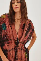 Vestido midi de viscosa con escote en V profundo, mangas cortas tipo kimono y cintura elástica con lazo ajustable. Presenta un estampado tie-dye en tonos rojizos, negros y toques de verde, con aplicaciones decorativas brillantes.