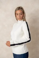 Buzo de punto acanalado color beige, con cuello alto, corte oversize y mangas largas. Presenta costuras decorativas en color negro que recorren los hombros y las mangas.