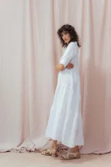 Vestido midi blanco de lino, con cuello camisero, botonera frontal y mangas 3/4. Presenta un calce relajado con frunces en la cintura.