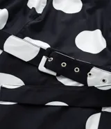 Vestido midi de algodón con estampado de lunares blancos sobre fondo negro. Presenta escote en V, mangas cortas abullonadas, cintura ajustada con cinturón de hebilla y falda con tajo lateral.