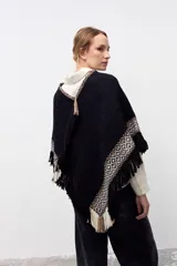 Poncho artesanal de lana en color negro, con diseño de guardas geométricas en tonos beige y blanco en los bordes y flecos decorativos en todo el contorno.