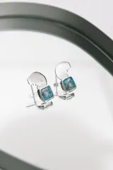 Par de aros de plata con forma geométrica y piedra cuadrada color celeste.
