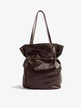 Bolso tipo tote de cuero vacuno marrón, de gran tamaño y diseño liviano. Cuenta con doble asa de hombro y detalle de correa ajustable con nudo en el frente.