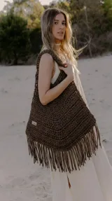 Bolso de mano grande tipo tote bag tejido a crochet con técnica artesanal. El material es trapillo reciclado, grueso y suave, con flecos largos en el borde inferior. El color es marrón oscuro (visón/óxido).