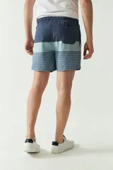 Short de baño celeste con rayas verticales blancas, cintura elástica con cordón ajustable, dos bolsillos laterales y uno trasero.