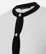 Cardigan de punto color blanco con detalles en negro en cuello, puños y tapeta frontal. Presenta cierre frontal con botones perlados y dos bolsillos delanteros falsos con solapa bicolor.