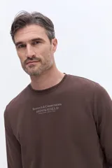 Remera de manga larga Brooksfield color marrón, con cuello redondo y textura sutil. Presenta un estampado frontal con el logo y leyenda de la marca.