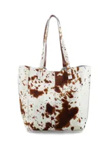 Cartera shopper confeccionada en cuero con pelo con estampado animal print tipo vaca en tonos blancos y marrones, con doble asa de hombro y bolsillo interior con cierre.