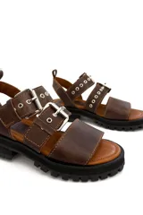 Sandalias de cuero color marrón chocolate, con tres tiras horizontales con ojales y hebillas metálicas plateadas. Suela de goma negra con plataforma.