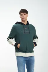 Canguro marrón con capucha forrada en verde oscuro, cordones de ajuste y bolsillo tipo canguro. Las mangas son largas, con puños verdes y franjas horizontales blancas y verdes.