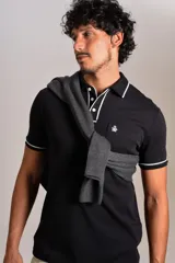 Polo de manga corta confeccionado en tejido interlock suave, color negro con detalles de vivos en color blanco en el cuello y las mangas. Presenta tapeta con botones y un bolsillo frontal con el logo bordado.