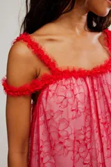 Vestido corto de tul bordado color rojo y rosado, con escote recto, volados sobre los hombros, tiras finas regulables y ruedo terminado en volado. Caída suelta y liviana.