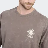 Remera de algodón color beige con efecto lavado, de corte holgado y manga corta. Presenta un pequeño logo estampado en el pecho con diseño de sol y el nombre de la marca.