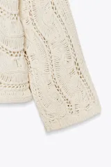 Sweater color crudo de punto calado con cuello barco y manga larga acampanada.