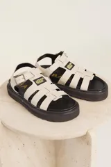 Sandalias de tiras anchas color crema con ajuste de hebilla al tobillo y suela track negra.