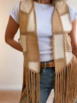 Chaleco de diseño patchwork en tonos neutros con efecto gamuza y pespuntes decorativos, abierto al frente y con largos flecos colgantes en el bajo.