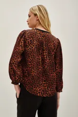 Camisa de manga larga con estampado animal print en tonos caramelo y negro. Presenta un escote en V con una solapa central en color negro y puños elásticos.
