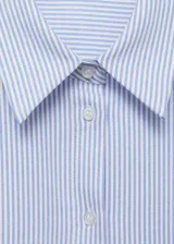 Camisa celeste a rayas verticales blancas, de corte recto, manga larga con puños abotonados, cuello camisero y bolsillo de parche en el pecho.