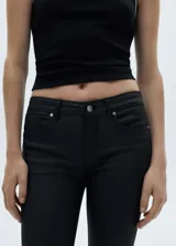 Pantalón jeans tipo skinny con acabado encerado, tiro bajo y diseño de cinco bolsillos. Confeccionado en tejido elástico con cierre de cremallera y botón.