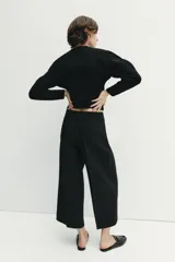 Pantalón culotte negro de tiro alto con bolsillos delanteros, pernera ancha y corta, y raya marcada al frente. Cuenta con cierre lateral con cremallera oculta.